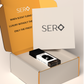 corner view of a packaging within it a minimalist clear glass perfume bottle with black wood cap containing SERO fragrance inspired by TOM FORD's Ombré Leather. 