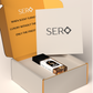 Corner view of a packaging within it a minimalist clear glass perfume bottle with black wood cap containing SERO fragrance inspired by Parfums de Marly Althaïr. 
